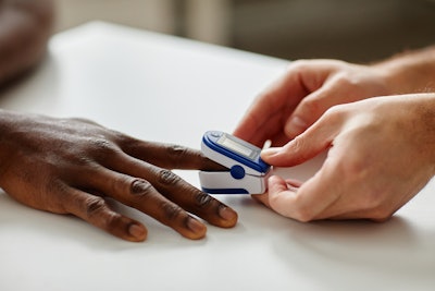 Image of pulse oximeter on patient hand being examined by doctor
