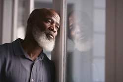 Photo of elderly black man looking depressed leaning against window