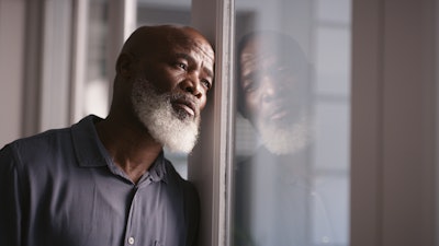 Photo of elderly black man looking depressed leaning against window
