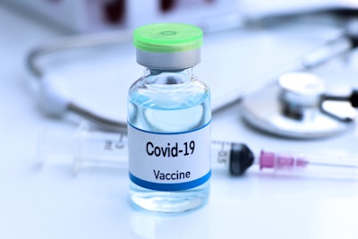 Phot of COVID-19 vaccination vial with needle in background