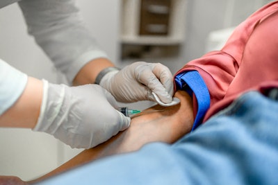 Nurse drawing blood from a female patient's arm vein in the medical clinic.