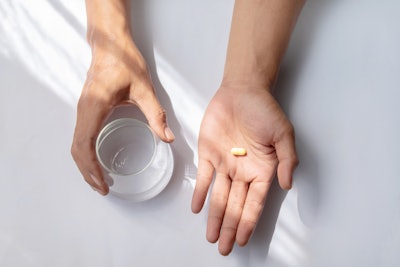 Asian man holding pill and a glass of water.