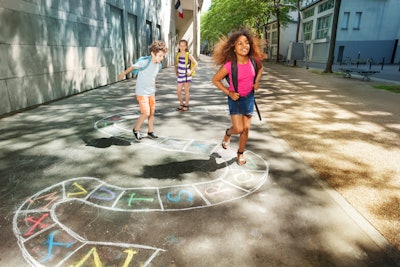 A diverse group of kids is playing outside an urban school setting.