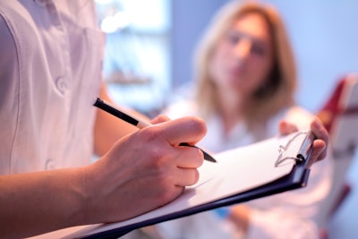 Image of a doctor writing on a clipboard with an out of focus woman in the background.