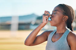 A woman using an inhaler outdoors.