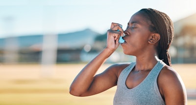 A woman using an inhaler outdoors.