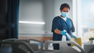 A Black, female nurse is cleaning a hospital bed.