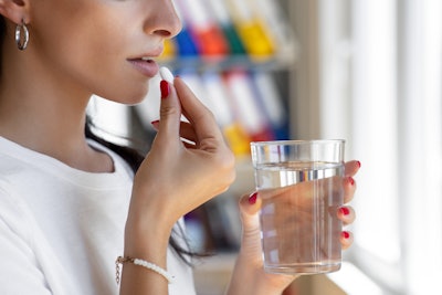 Woman taking tablet with glass of fresh water.
