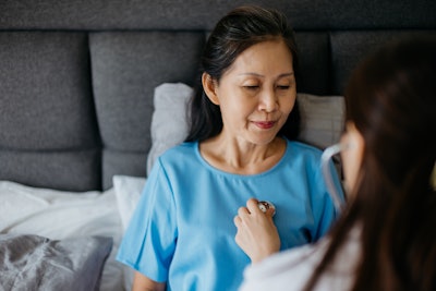 Female doctor using a stethoscope to examining patient's lung and heartbeat during a health care home visit.