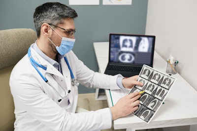 Doctor wearing a protective face mask analyzes results of a patient's lungs CT scan at a medical clinic.