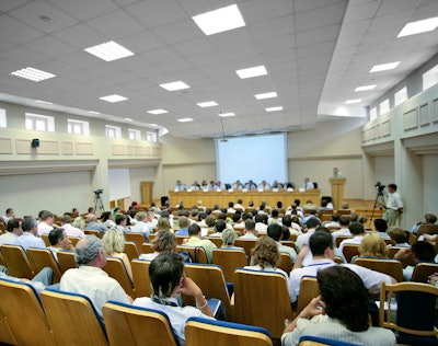 A panel of speakers is speaking to a large audience at a scientific conference.