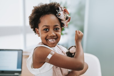 A young, Black girl shows off her bandaid after an injection in the doctor's office.