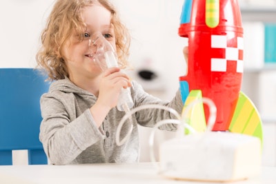 Happy child with oxygen mask receiving cystic fibrosis treatment and playing with toy rocket.