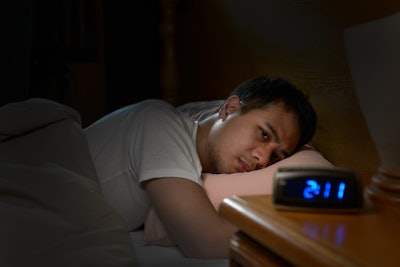 A man with insomnia is lying awake in bed with the alarm clock reading 2:11 a.m.