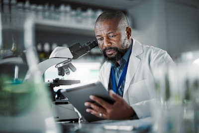 Black doctor examining a tablet next to a microscope.