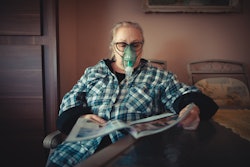 An older woman pictured with an oxygen mask receiving ventilation treatment.