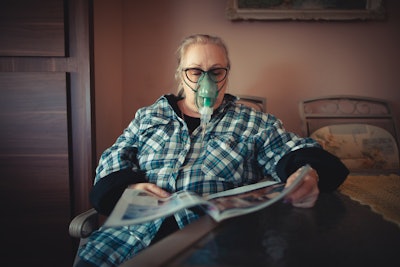 An older woman pictured with an oxygen mask receiving ventilation treatment.