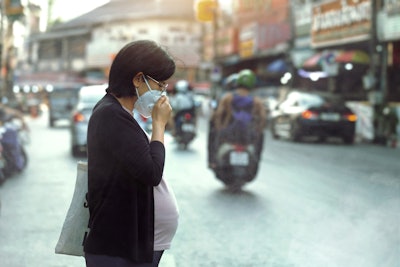 Asian pregnant woman in the middle of the road wears a PM2.5 dust mask to protect against pollution.