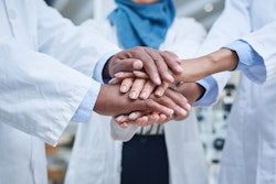 A group of unrecognizable scientists joining hands in solidarity in a laboratory.