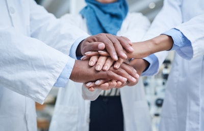 A group of unrecognizable scientists joining hands in solidarity in a laboratory.