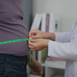 This is a photo of a medical professional measuring the diameter of a man's waist with measuring tape.