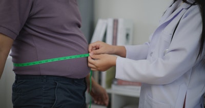 This is a photo of a medical professional measuring the diameter of a man's waist with measuring tape.