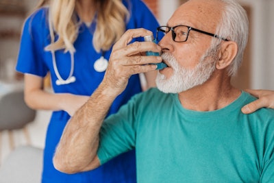 Older man using an inhaler with female medical professional in the backround.