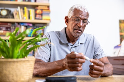 This is a photo of an older, Black man testing his blood sugar with a finger stick.