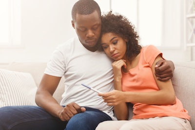 This is a photo of a sad Black family looking at a pregnancy test and learning they are not pregnant.
