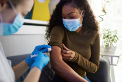 Young African American woman wearing a protective mask receives vaccination.