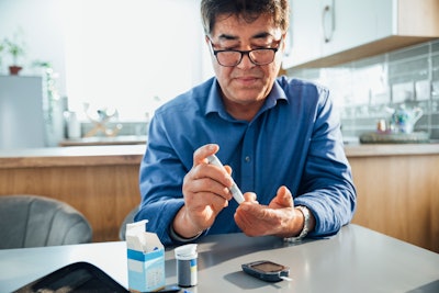 This is a photo of an Asian man pricking his finger to test his blood sugar for diabetes.