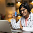 Female Indian American doctor holds inhaler during virtual appointment on a laptop.