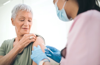 Health care worker gives vaccine to older woman.