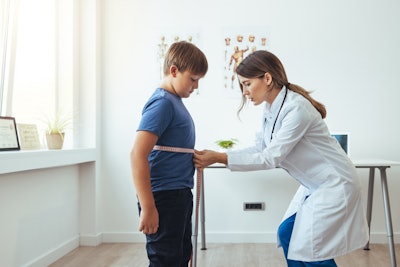 Female nutritionist measuring waist of young patient by tape indoors in the office