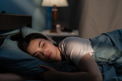 This is a photo of a young, white woman lying awake in bed with insomnia.