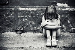 Black and white photo of a depressed child sitting on a worn sidewalk.