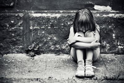 Black and white photo of a depressed child sitting on a worn sidewalk.