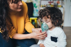 Female adult helps small child with RSV use nebulizer.