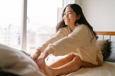 This is a photo of a young, Asian woman waking up refreshed and strecthing.