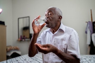 Elderly man taking a pill while sitting on a bed.