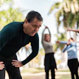 This is a photo of a man bent over and struggling to catch his breath while people behind him are exercising,.