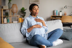 This is a photo of a young, Black, pregnant woman sitting on the couch and breathing deeply.