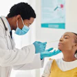 This is a photo of a Black, male health care worker swabbing the inside of a middle school, Black, female girl.