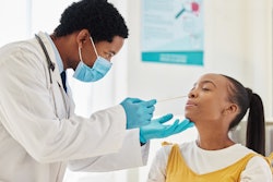 This is a photo of a Black, male health care worker swabbing the inside of a middle school, Black, female girl.