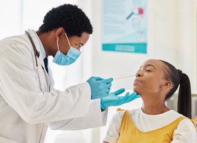 This is a photo of a Black, male health care worker swabbing the inside of a middle school, Black, female girl.