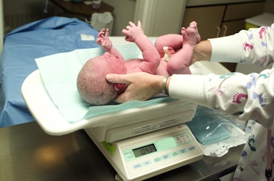 Image of a newborn baby being weighed on a scale.