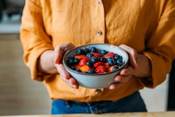 This is a photo of a person holding a bowl of berries with two hands. No face is displayed.