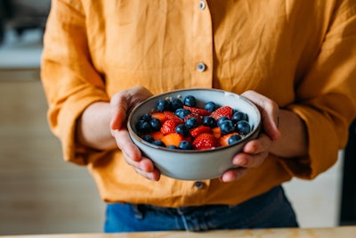 This is a photo of a person holding a bowl of berries with two hands. No face is displayed.