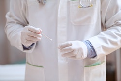 Medical professional in white holding a cotton swab for testing.