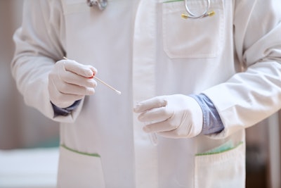 Medical professional in white holding a cotton swab for testing.